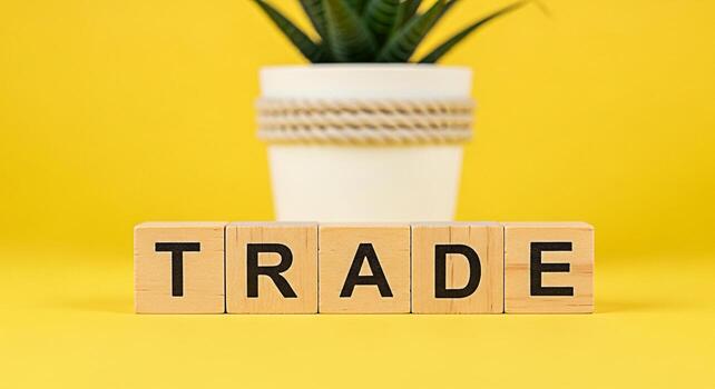 Wooden blocks spelling out TRADE on a vibrant yellow surface symbolizing global commerce and financial transactions with a potted succulent plant in the background creating a modern and optimistic bus photo