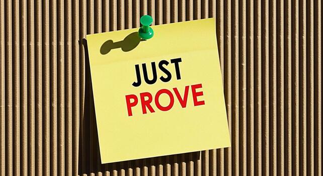 Yellow sticky note displaying the words Just Prove attached to a cardboard surface with a green pushpin conveying a message of challenge motivation and the need for validation in a business or persona photo