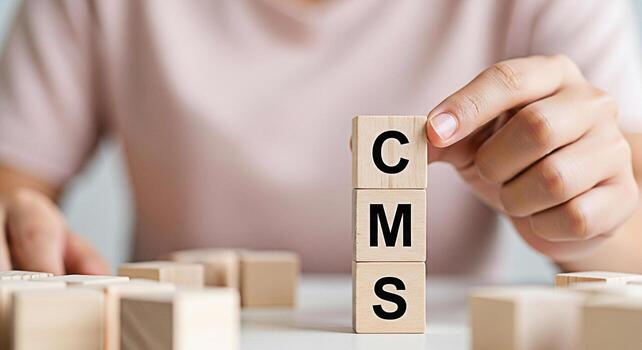 Person arranging wooden blocks with the letters CMS on a white table representing content management system strategy and solutions for online business success conveying a message of organization and c photo