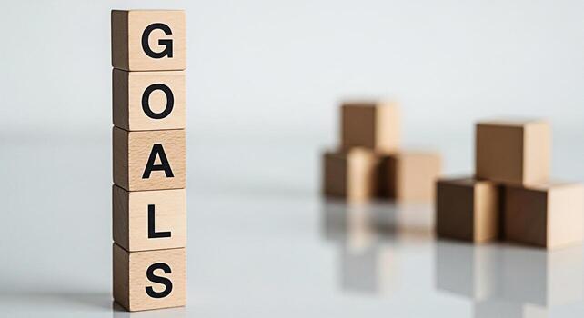 Wooden blocks stacked vertically spelling GOALS on a reflective surface with blurred blocks in the background representing ambition and achievement in a minimalist clean and focused environment photo