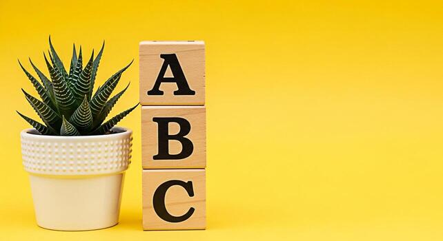 Wooden alphabet blocks stacked next to a potted succulent plant against a vibrant yellow backdrop creating a playful and educational scene symbolizing learning growth and a bright optimistic future photo