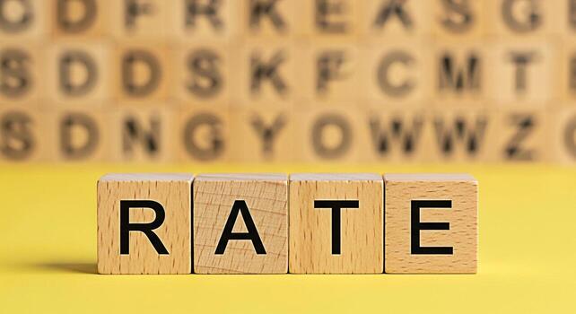 Wooden blocks spelling RATE on a bright yellow surface with blurred alphabet blocks in the background representing interest rates financial calculations and the concept of evaluating performance photo
