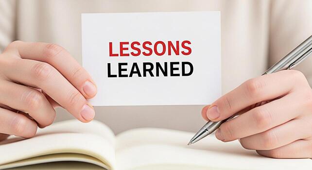 Closeup of hands holding a card with the words Lessons Learned while taking notes in a notebook with a pen in a bright neutraltoned setting emphasizing the concept of reflection and continuous improve photo