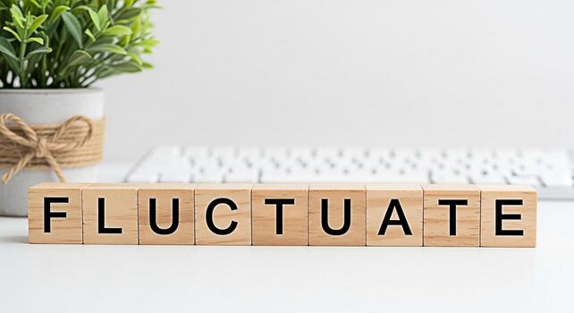 Wooden blocks spelling Fluctuate on a white desk with a keyboard and potted plant representing market volatility and the dynamic nature of business conveying a sense of uncertainty and change in a mod photo