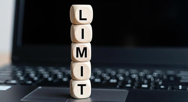 Wooden dice spelling LIMIT stacked on a laptop keyboard symbolizing constraints and boundaries in the digital workspace conveying a message of setting limitations and managing digital distractions for photo
