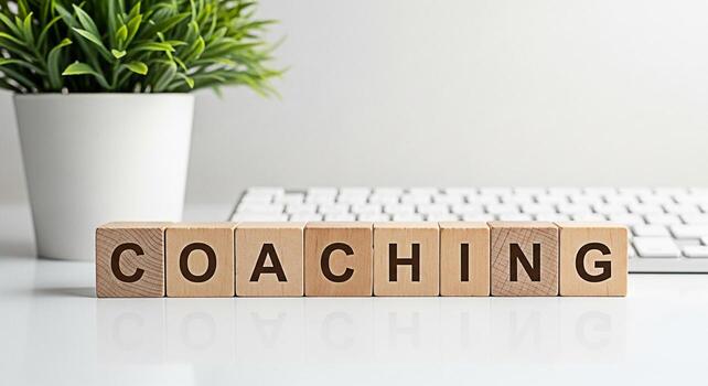 Wooden blocks spelling Coaching on a white desk with a keyboard and a potted plant representing guidance and support in a modern office environment fostering growth and development with a minimalist a photo