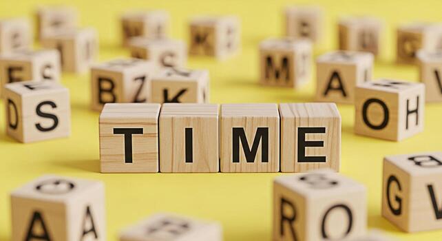 Wooden blocks spelling TIME on a yellow surface surrounded by other lettered blocks symbolizing the importance of time management deadlines and the fleeting nature of time in a playful and educational photo