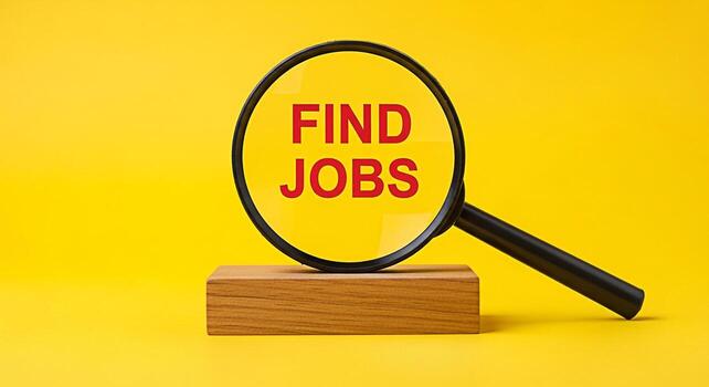 Magnifying glass focusing on Find Jobs text placed on a wooden block against a bright yellow background symbolizing job searching and career opportunities with a hopeful and optimistic mood photo