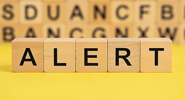 Wooden blocks spelling ALERT on a bright yellow surface conveying a sense of urgency and importance with blurred letter blocks in the background emphasizing the need for attention and immediate action photo