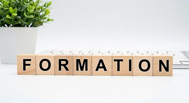Wooden blocks spelling FORMATION resting on a white desk with a keyboard and a green plant conveying a concept of business strategy team building and organizational structure in a clean modern setting photo