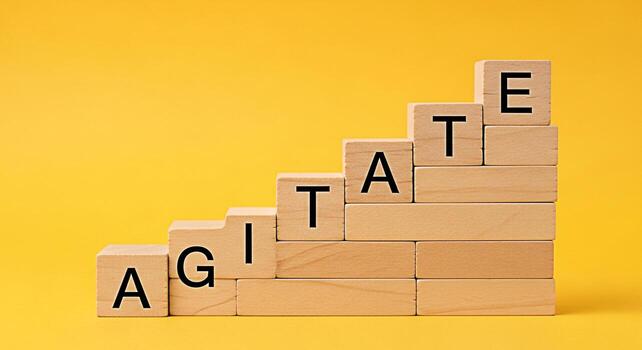 Wooden blocks spelling AGITATE arranged in a staircase pattern against a vibrant yellow background symbolizing stirring up emotions or discussions creating a sense of urgency and action photo