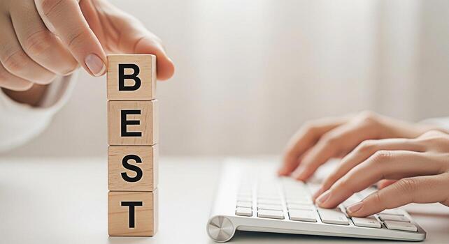 Person stacking wooden blocks spelling BEST while typing on a keyboard in a bright minimalist office setting symbolizing success achievement and striving for excellence in business and personal goals photo