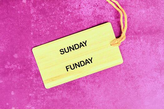 A light yellow tag with SUNDAY FUNDAY on it rests on a textured magenta surface, held by a string, implying a day full of laughter and good times is coming photo