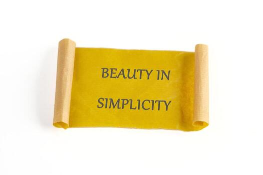A warm yellow scroll with the phrase beauty in simplicity elegantly displayed in dark letters. The simple design highlights the charm of minimalism against a clean, white background photo