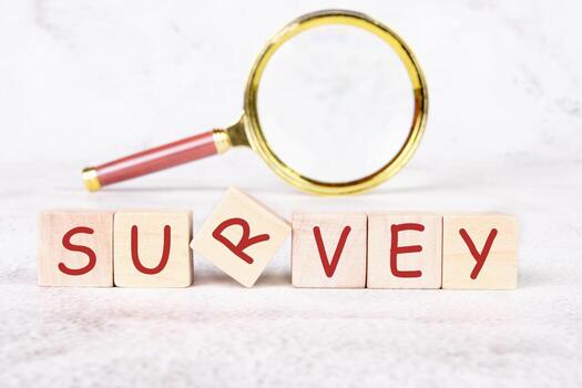 Wooden blocks spell out SURVEY, with one block slightly askew. A gold magnifying glass rests nearby. Analysis and planning concept for improved performance are suggested photo