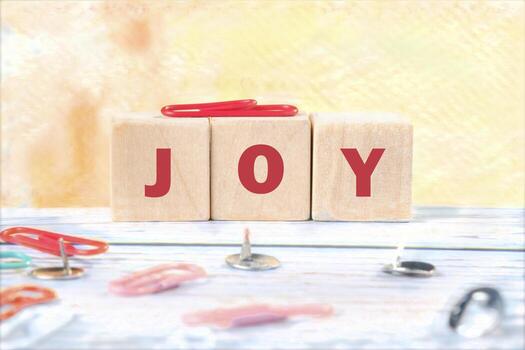 Wooden blocks display the word joy in bold red letters, surrounded by colorful paper clips on a light, softly colored surface, creating a cheerful atmosphere photo