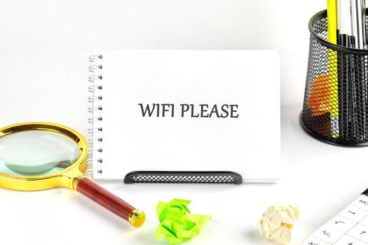 A notepad displays the words WIFI PLEASE next to a magnifying glass, crumpled paper, pens, and calculator suggesting a search for connection and productivity photo