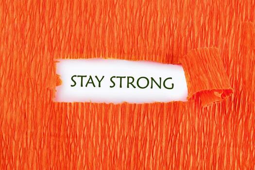 Text reads STAY STRONG, showing through a tear in bright orange crepe paper. It offers a message of resilience and motivation for someone facing adversity photo