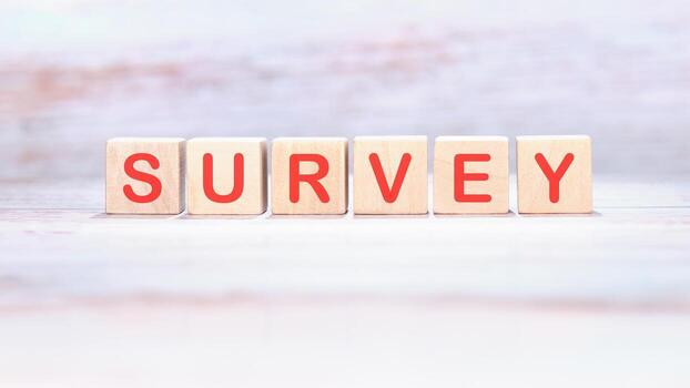 Wooden blocks, each displaying a red letter, spell out SURVEY. The blocks sit neatly aligned on a textured white surface, inviting participation and input photo