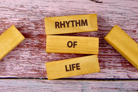 Wooden blocks display the phrase RHYTHM OF LIFE arranged centrally against a weathered wood surface. Other blocks are scattered adding depth and echoing lifes cycles photo