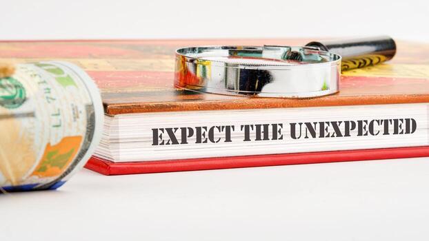 Expect The Unexpected word on the end of the book on a white background and compositions with a magnifying glass and money photo