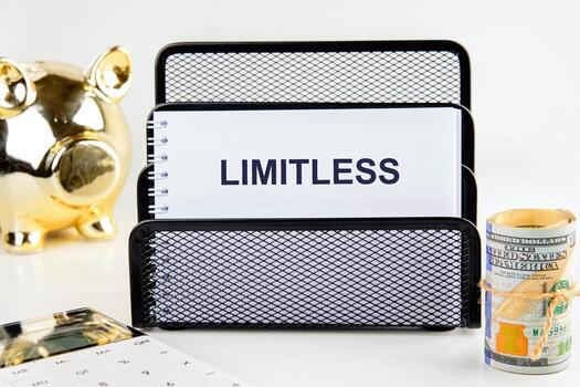 A neatly organized workspace features a black mesh file holder with a notepad that reads LIMITLESS, a gold piggy bank, a stack of cash, and a calculator, symbolizing financial growth photo