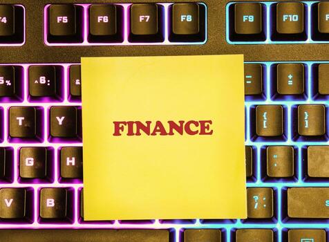 Bright yellow sticky note displays the word finance on a keyboard illuminated in vibrant colors, capturing a moment of study and concentration in a modern workspace setting photo