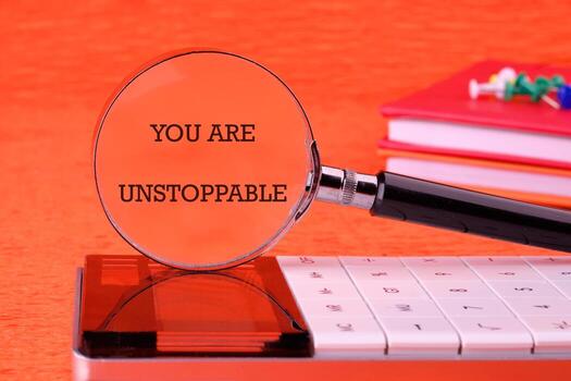 Concept text YOU ARE UNSTOPPABLE focused through a magnifying glass on an orange background, based on a calculator photo
