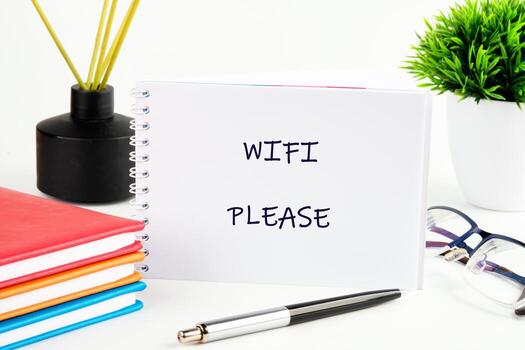 A cozy workspace features a note requesting wifi, surrounded by colorful notebooks, a sleek pen, and a touch of green foliage, inviting creativity and connection photo