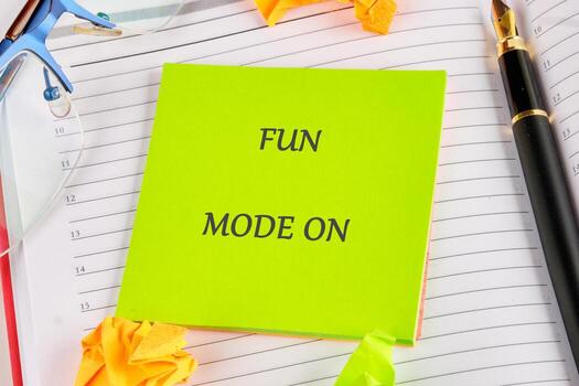A bright green sticky note with bold text announces fun mode is activated. Surrounded by crumpled paper and writing instruments, it creates a vibrant workspace atmosphere photo