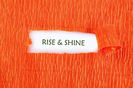 An orange textured material is torn open, revealing the phrase RISE SHINE printed on a white background underneath. It conveys a message of positivity and optimism photo