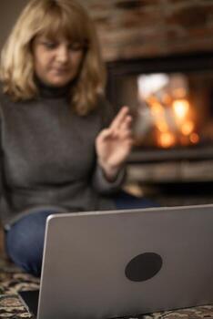 A woman makes a gesture during a call on her computer while sitting near the fireplace. photo