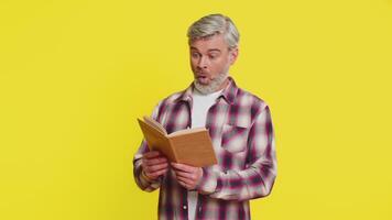 mogna man fokuserar spänt på öppen bok avslöjande bedövad nyfikenhet förvirrad blick. medelålders kille på gul bakgrund utställningar förvånad Wow reaktion, antyda på ny uppenbarelser dold i text video
