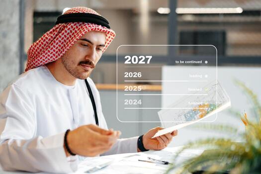 Man in traditional attire working on project timelines in modern office setting photo