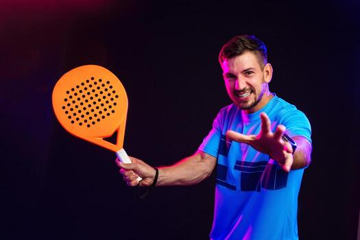 Man playing padel with an orange racket in a dark setting during a sports event photo