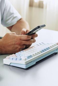 Person using smartphone while sitting at desk with a colorful keyboard photo