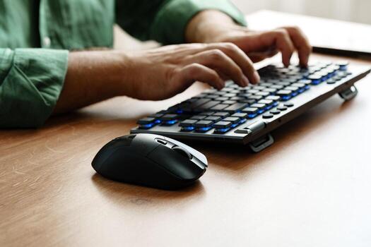 Person typing on a modern keyboard while using a computer mouse at a wooden desk photo