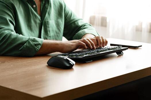 Person using a computer keyboard while sitting at a wooden desk in a well-lit room photo