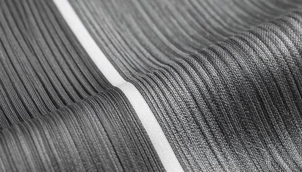 Close-up shows the intricate texture of a ribbed grey fabric with a bright white stripe running vertically across the surface of the material. photo
