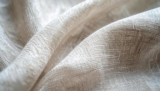 Close up of a folded beige linen textile shows a textured surface with interwoven threads creating soft shadows in a natural light setting. photo