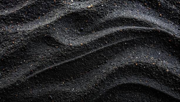 Dark grainy sand exhibits a textured, wave-like pattern across the surface, creating an abstract, organic background for various applications. photo