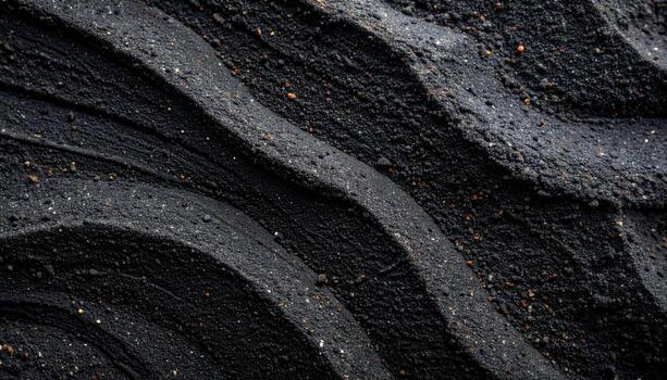 The dark sand of a volcanic beach shows layered textures with curved patterns creating an abstract background of natural earth formations. photo