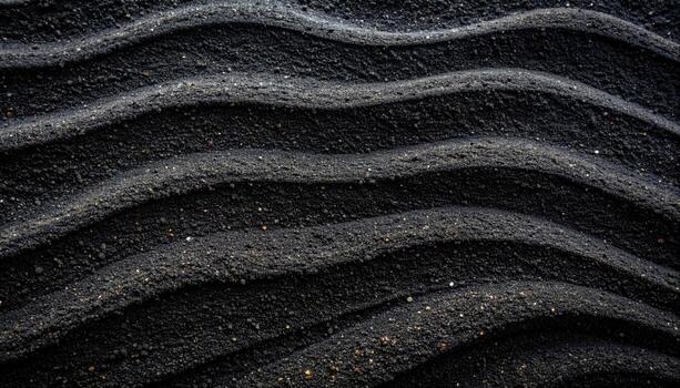 Black sand waves create a rhythmic pattern, displaying texture and form in an abstract natural background with subtle light and shadow play. photo