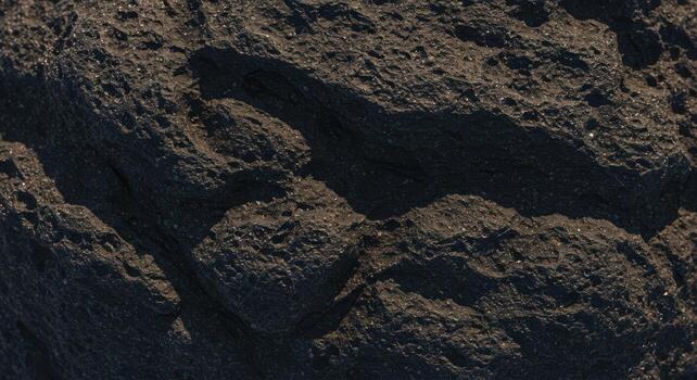 Close up of rugged and textured dark grey volcanic rock surface with rough and uneven terrain, ideal for geological study or abstract background. photo