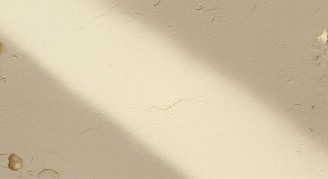 A diagonally cast light illuminates a textured cream colored wall adding depth and creating a subtle contrast in brightness across the surface. photo