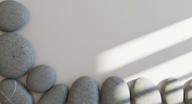 Smooth grey stones are arranged in a calming border formation over a plain surface with sunlight providing soft shadow lines across it all. photo