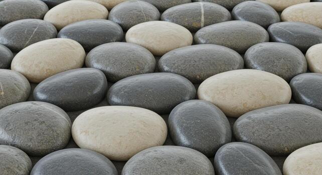 Close up image shows a pattern of smooth gray and tan stones arranged closely together creating a natural and calming visual texture design. photo