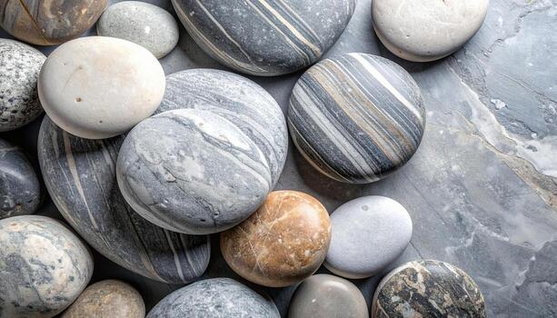 An overhead shot reveals a collection of smooth, rounded stones with diverse colors and patterns resting on a mottled stone surface background. photo