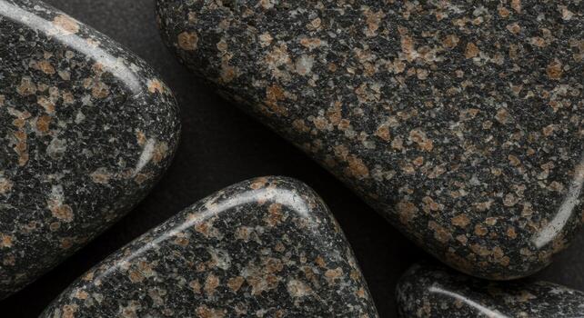 Close up shows smooth polished granite pebbles with brown and gray specks on dark background adding natural beauty and texture to composition. photo