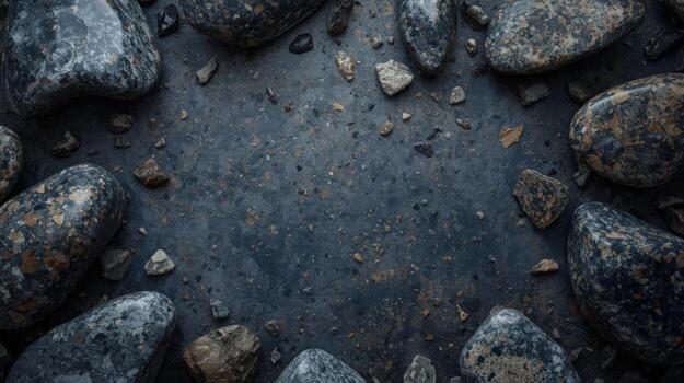 Dark river stones and pebbles are scattered around a textured slate surface creating a natural looking frame with copy space available here. photo